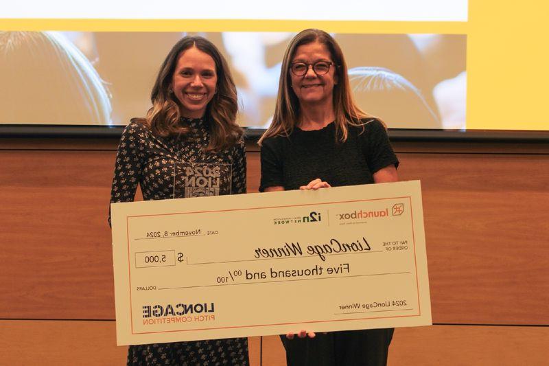 two women holding large checks